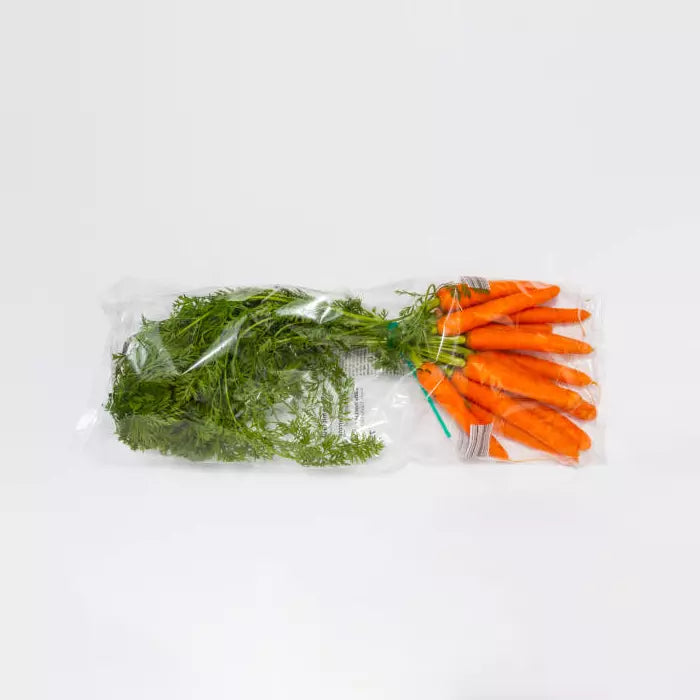 Bunch of carrots and dill in a clear plastic bag on a white background