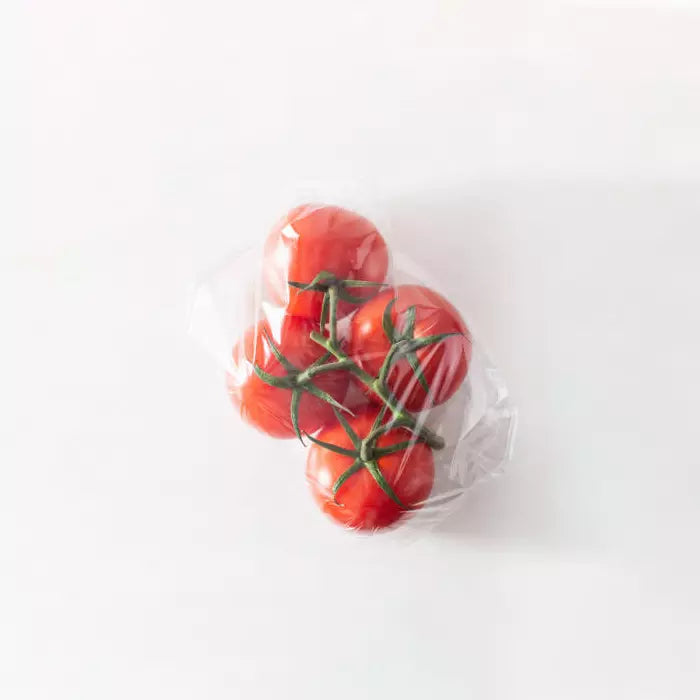 Three red tomatoes on a branch wrapped in clear plastic against a white background